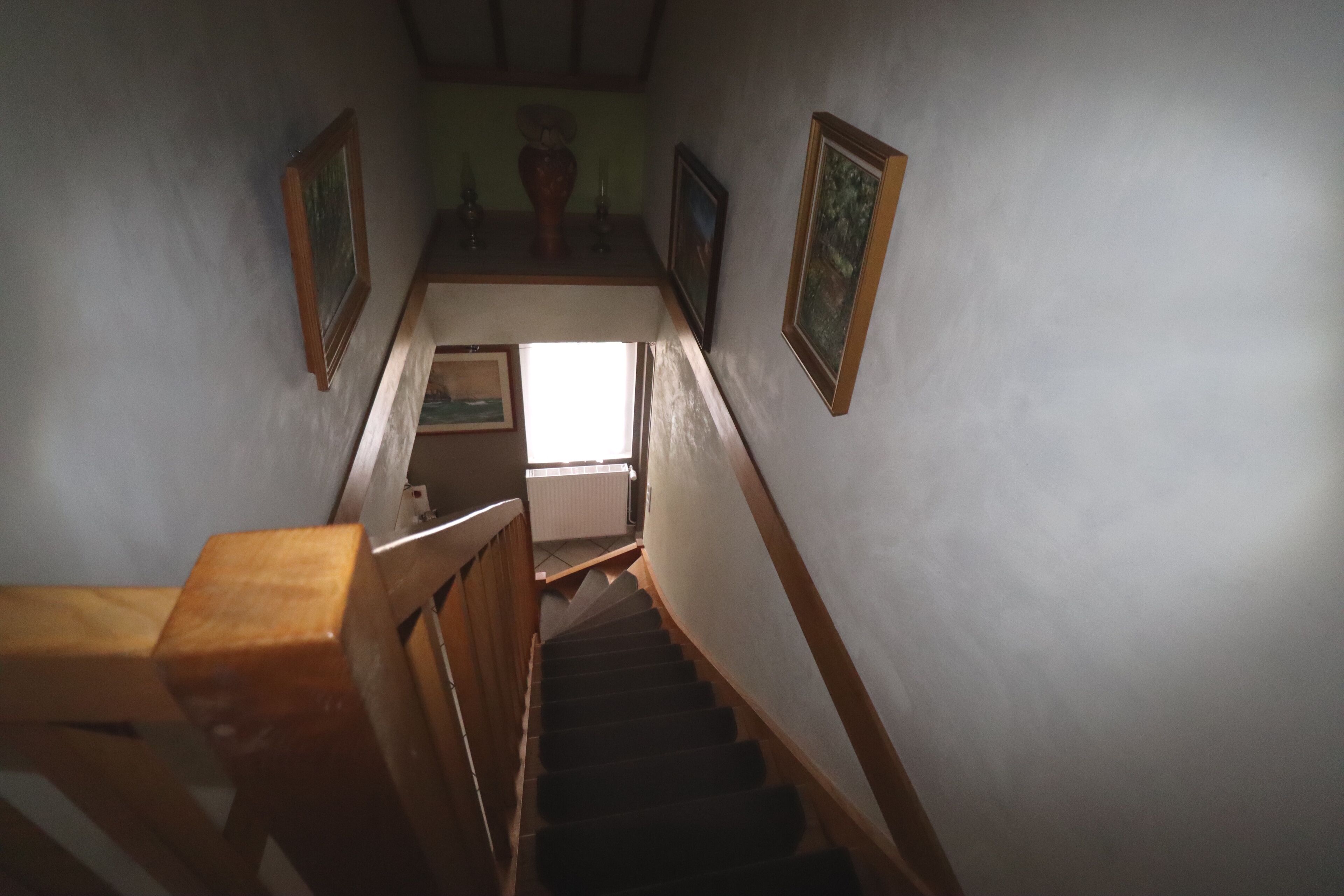 Una escalera con barandillas de madera, un radiador y cuadros enmarcados en las paredes.