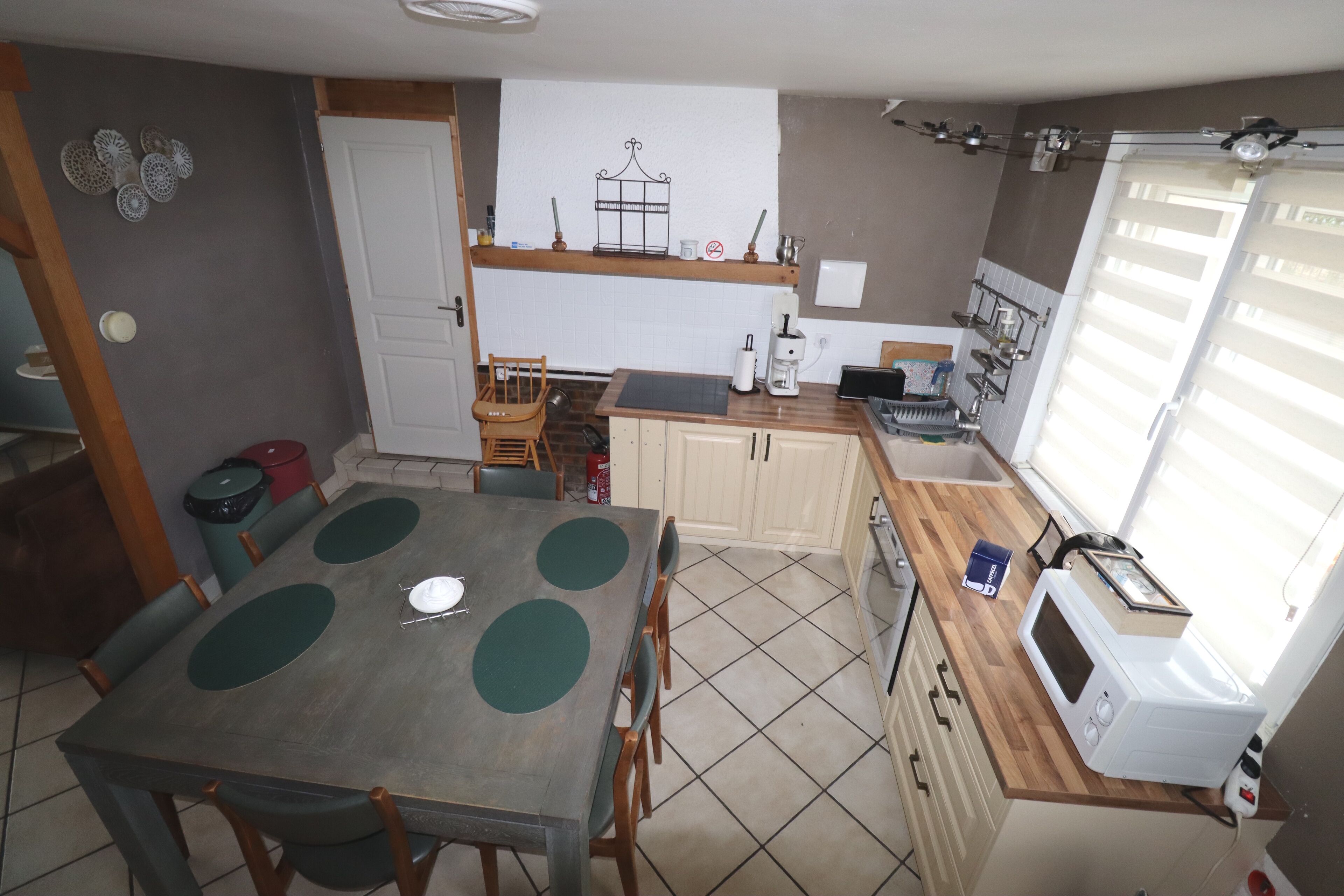 Une cuisine compacte comprenant une table à manger, un four à micro-ondes et une fenêtre avec des stores.