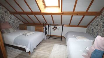 Une chambre avec deux lits, une lucarne, des poutres en bois, un papier peint à motifs et une petite armoire.