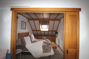 A bedroom with a sloped ceiling, a bed, a bedside table, and a window.