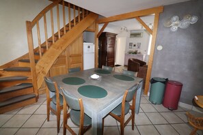 A dining area with a wooden staircase, a kitchen in the background, and two trash bins.