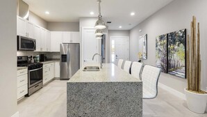 A modern kitchen with white cabinets, stainless steel appliances, granite countertops, and a central island.