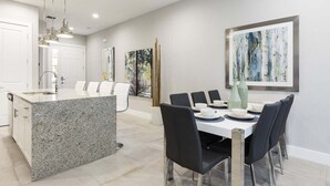 A modern kitchen with granite countertops, a dining area with a white table and black chairs, and artwork on the walls.