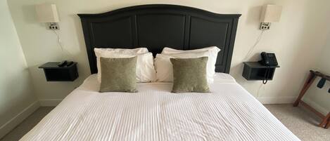 A neatly made bed with a green blanket and two white towels, a dark headboard, and a painting of a pier on the wall.