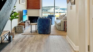 Un vaste espace de vie doté d’un plancher en bois, d’un escalier, d’une télévision et offrant une vue sur le port de plaisance.