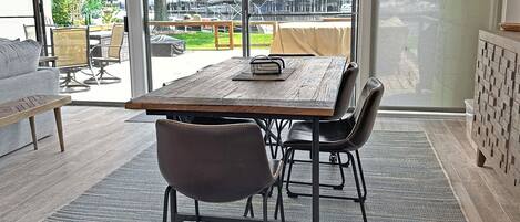 Un comedor moderno con una mesa grande y sillas, ventanas amplias con vista a un puerto deportivo y vegetación.
