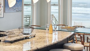 Een keuken met een groot eiland, barstoelen, hangende pendellampen en uitzicht op de oceaan.