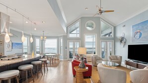 Een ruime woonkamer met een grote televisie, comfortabele zitplaatsen en uitzicht op de oceaan.
