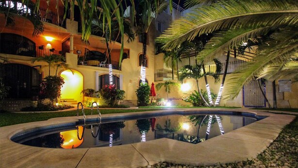 Una piscina con hidromasaje, rodeada de palmeras y un edificio con balcones.
