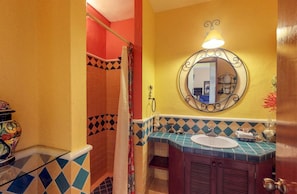 Un baño con un suelo de baldosas coloridas, un lavabo con espejo y una zona de ducha con cortina.