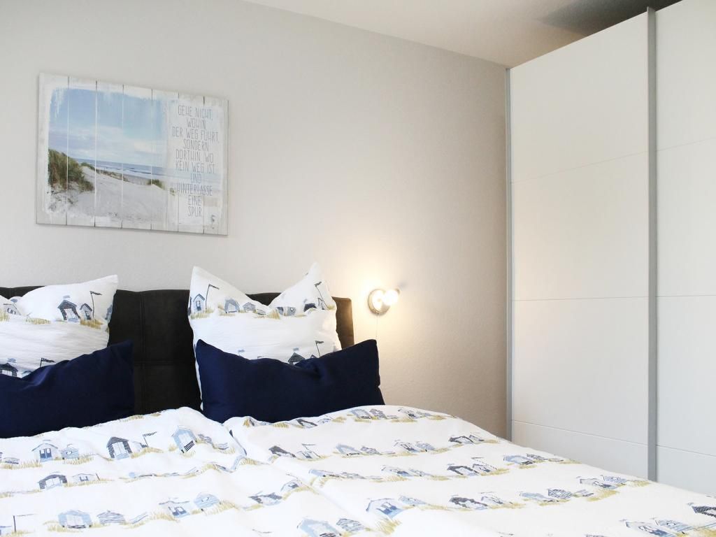 Une chambre à coucher avec un lit, des oreillers, une lampe fixée au mur et un tableau encadré.