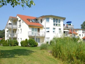 A multi-story residential building with balconies, a garden area, and a clear sky.