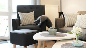 Un salon moderne avec un fauteuil noir, un canapé gris et une table basse blanche agrémentée d’un vase de fleurs.