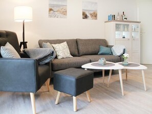 A modern living room with a grey sofa, a black armchair, a round coffee table, and a white cabinet with glass doors.
