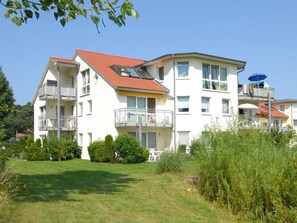Un immeuble résidentiel à plusieurs étages, doté de balcons, d’un espace jardin et offrant une vue sur un ciel dégagé.
