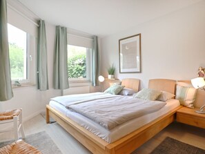 Une chambre à coucher avec un grand lit, des tables de chevet, une commode, une fenêtre avec des rideaux et un tableau encadré au mur.