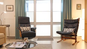 Een woonkamer met twee zwarte leren fauteuils, een glazen salontafel en een beige bank.