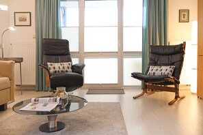 Un salon avec deux fauteuils en cuir noir, une table basse en verre et un canapé beige.