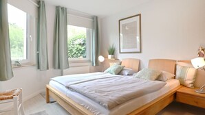 Een slaapkamer met een groot bed, nachtkastjes, een raam met gordijnen en een lijst met een afbeelding aan de muur.