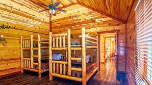 Interior de cabana rústica com beliches, piso de madeira e ventilador de teto.