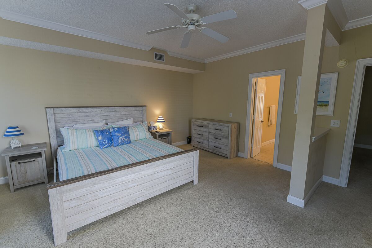 A bedroom with a bed, nightstands, a dresser, a ceiling fan, and a door leading to another room.