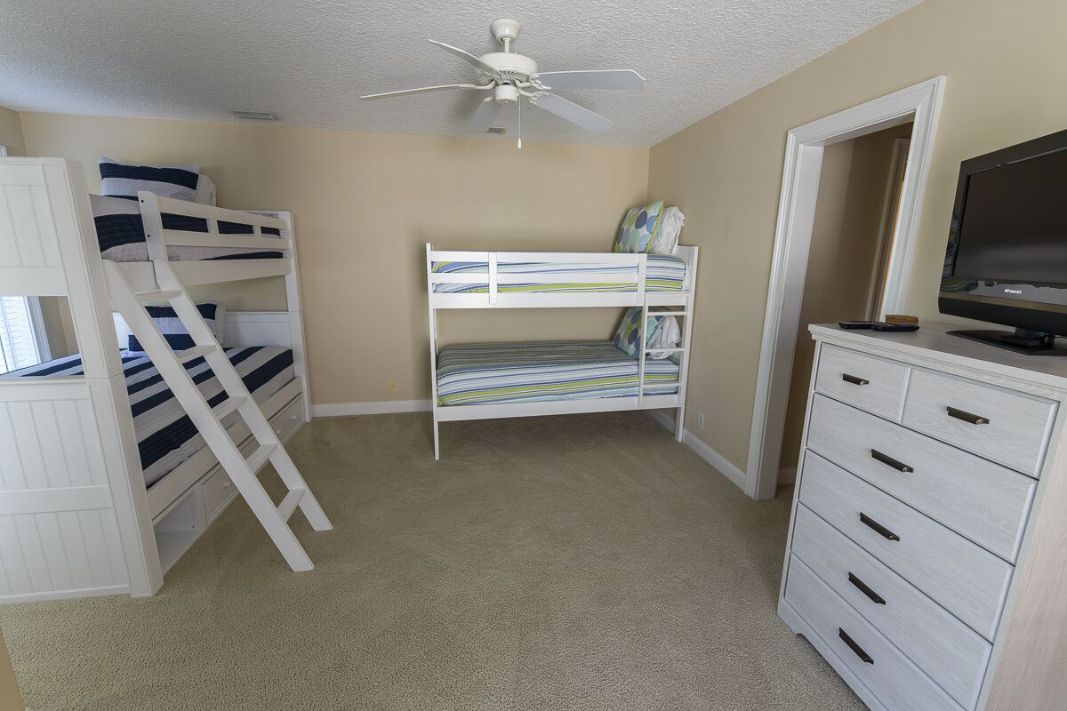A room with bunk beds, a ceiling fan, a TV, and a dresser.