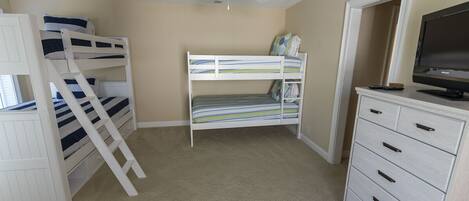 A room with bunk beds, a ceiling fan, a TV, and a dresser.