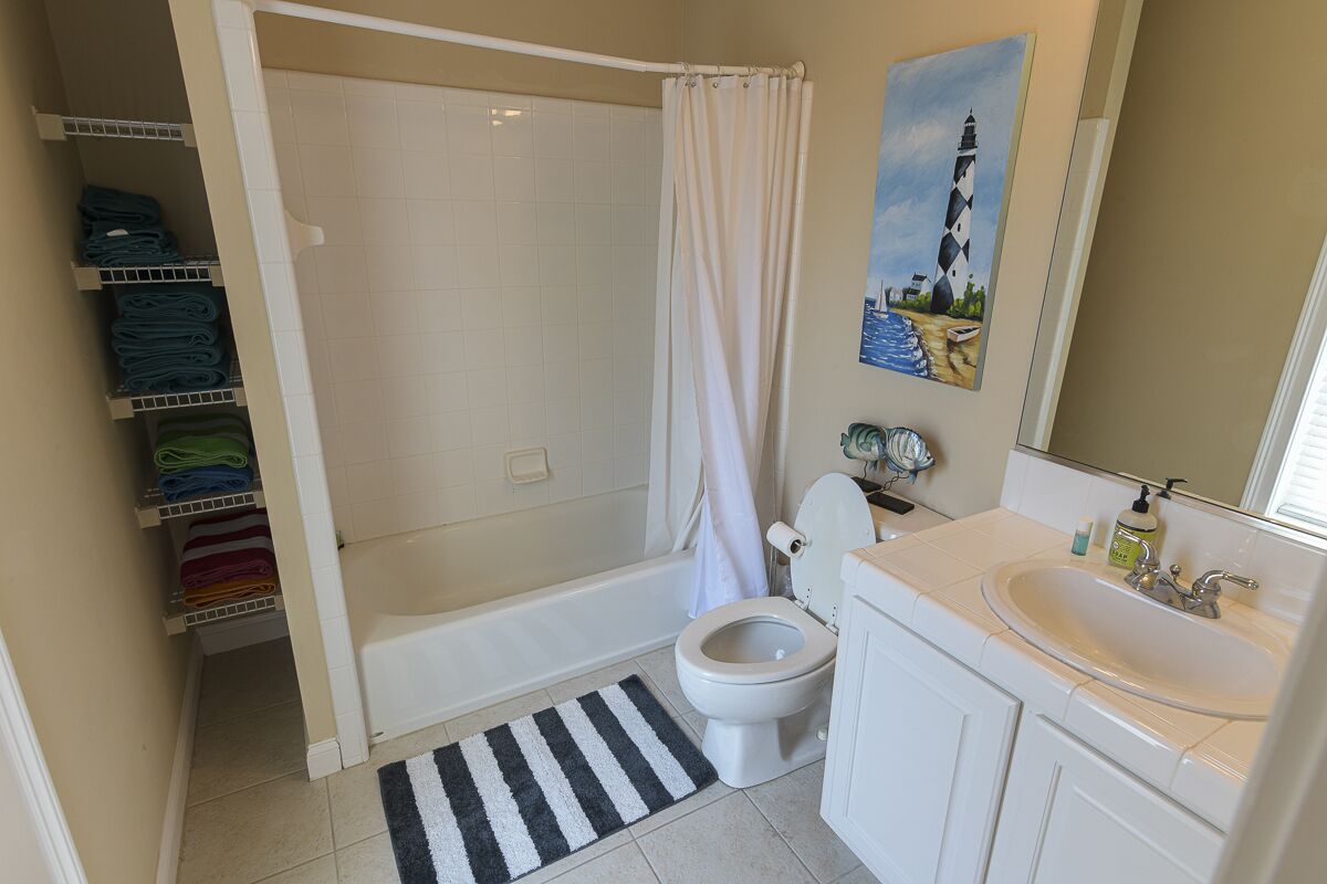 A bathroom with a bathtub, toilet, and sink. There is a striped rug on the floor and a painting on the wall.