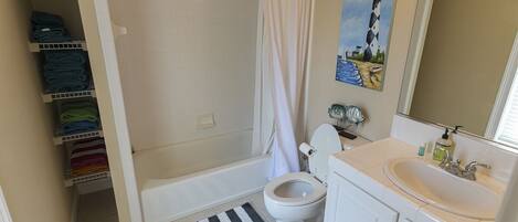 A bathroom with a bathtub, toilet, and sink. There is a striped rug on the floor and a painting on the wall.