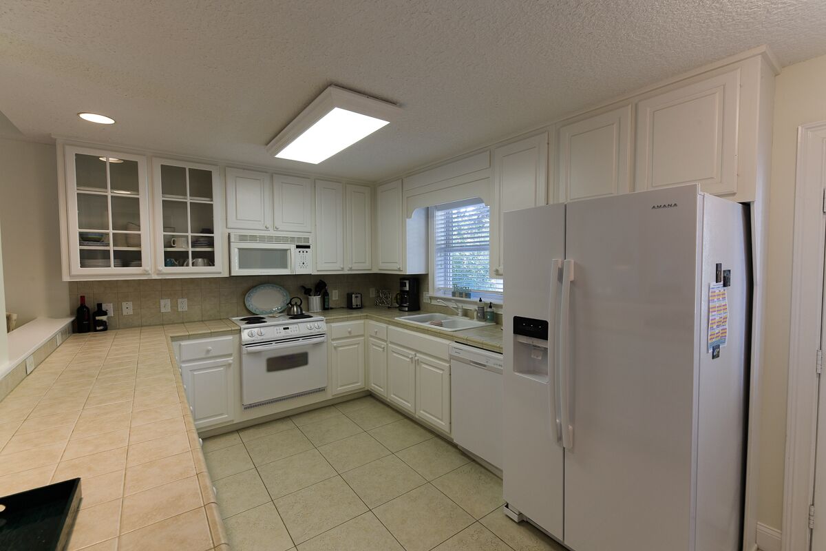 Una cocina con armarios blancos, estufa, horno, microondas, lavaplatos y refrigerador.