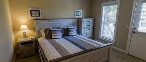 A bedroom with a bed, bedside tables, a nightstand, a dresser, a ceiling fan, and a window with blinds.
