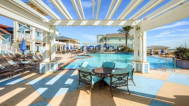 Zona de piscina con sillas de descanso y sombrillas, un espacio de estar techado y vistas a la piscina.