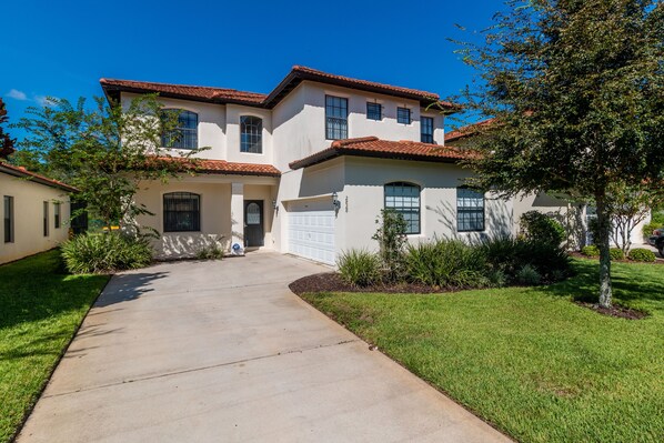 A two-story house with a tiled roof, a front garage, and a well-maintained lawn.