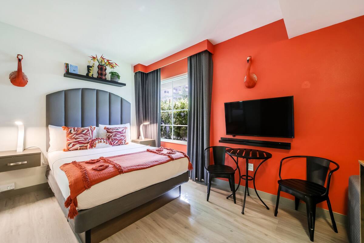 A modern hotel room with a large bed, a TV, a desk, and a chair.