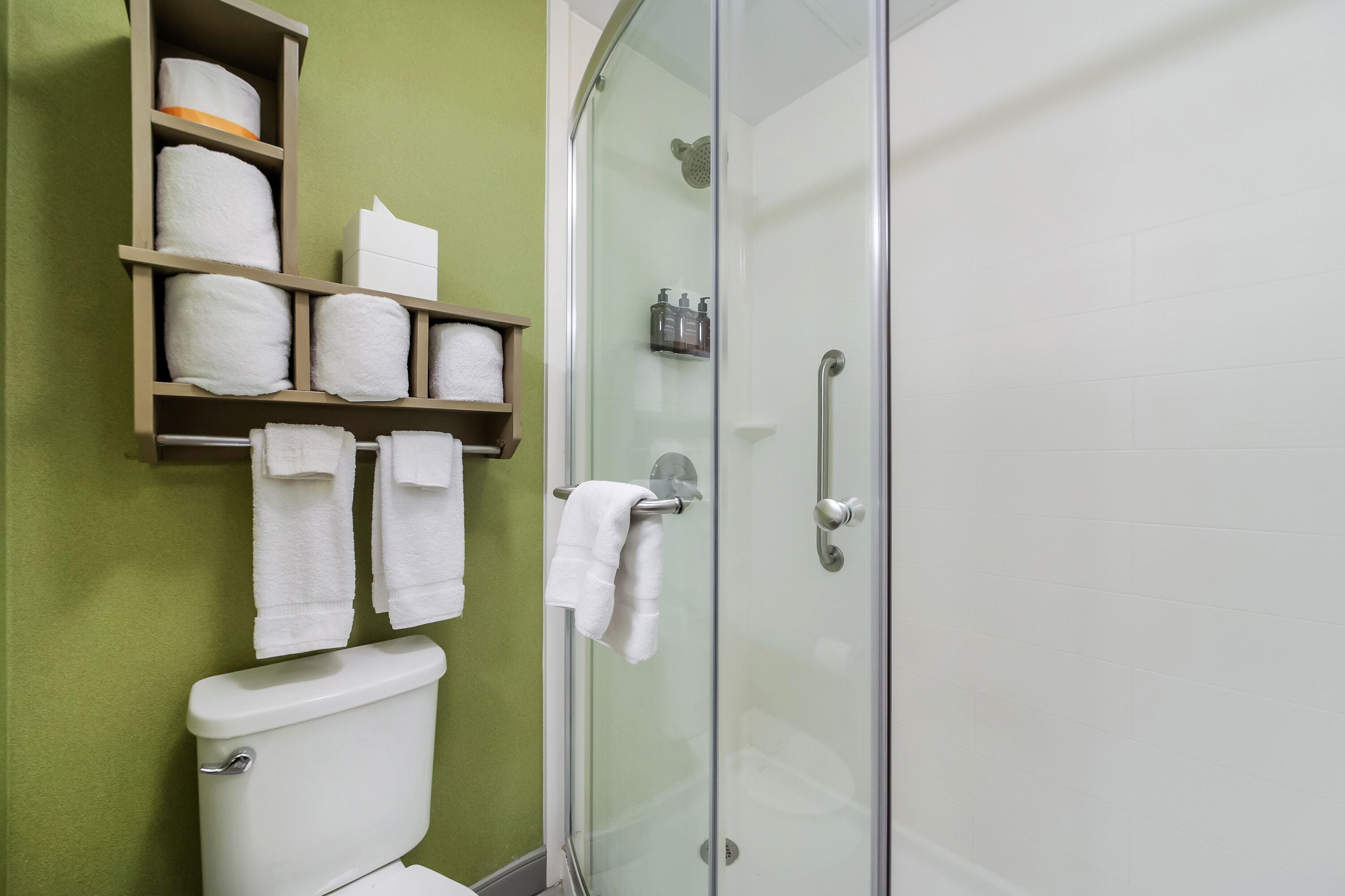 A bathroom with a toilet, a glass shower enclosure, and a shelf with towels.