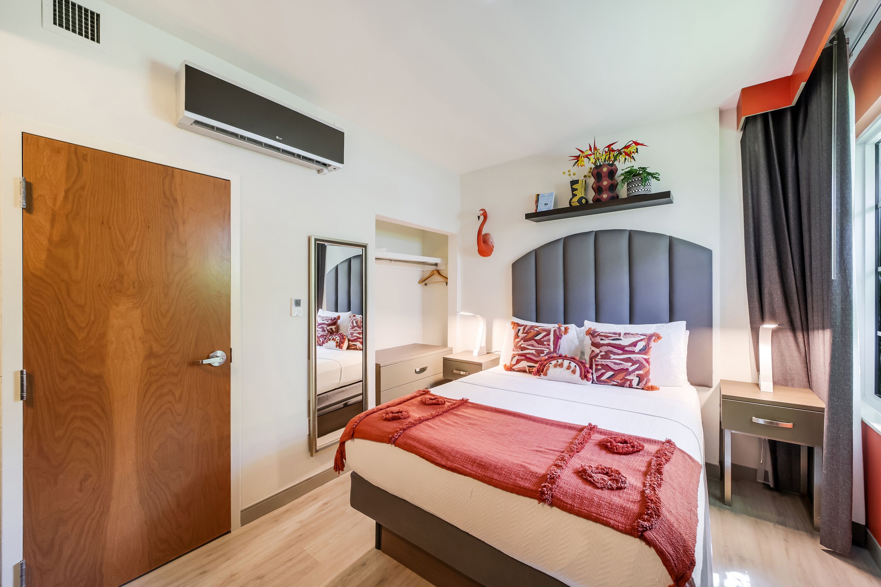 A modern hotel room with a large bed, bedside tables, a desk, and a mirror.