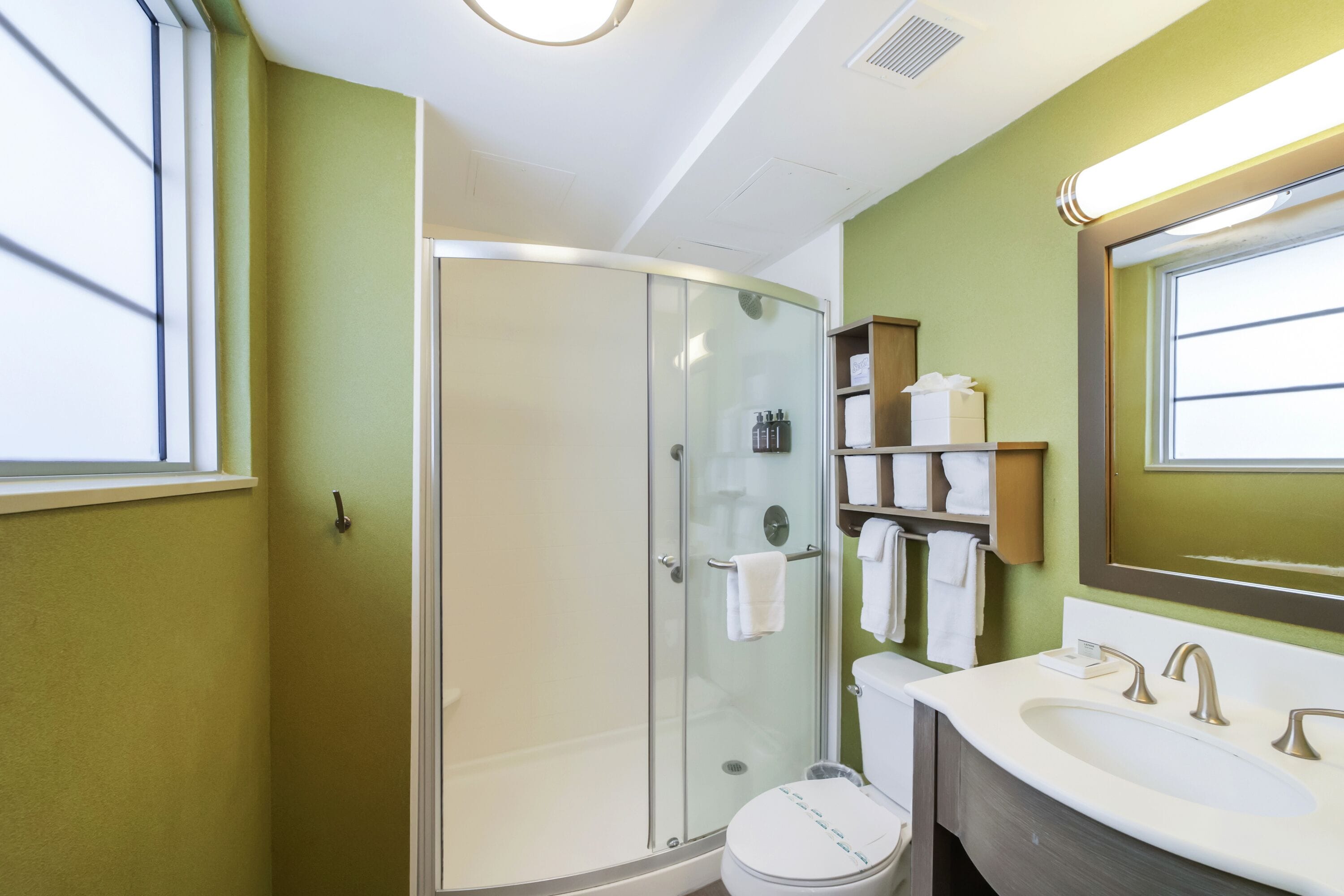 Un baño moderno con ducha envuelta en vidrio, inodoro blanco y tocador con lavamanos y espejo.