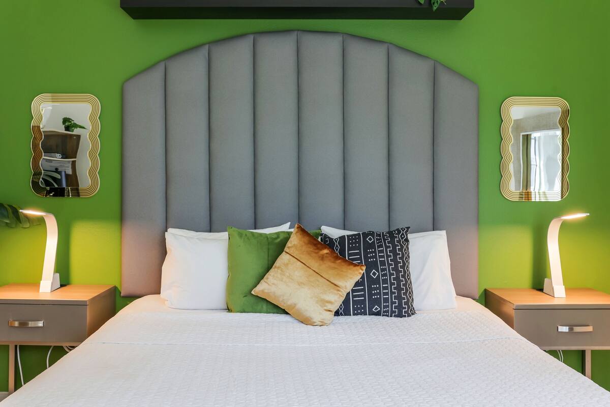 A neatly made bed with a grey headboard, two bedside tables with lamps, and green walls.