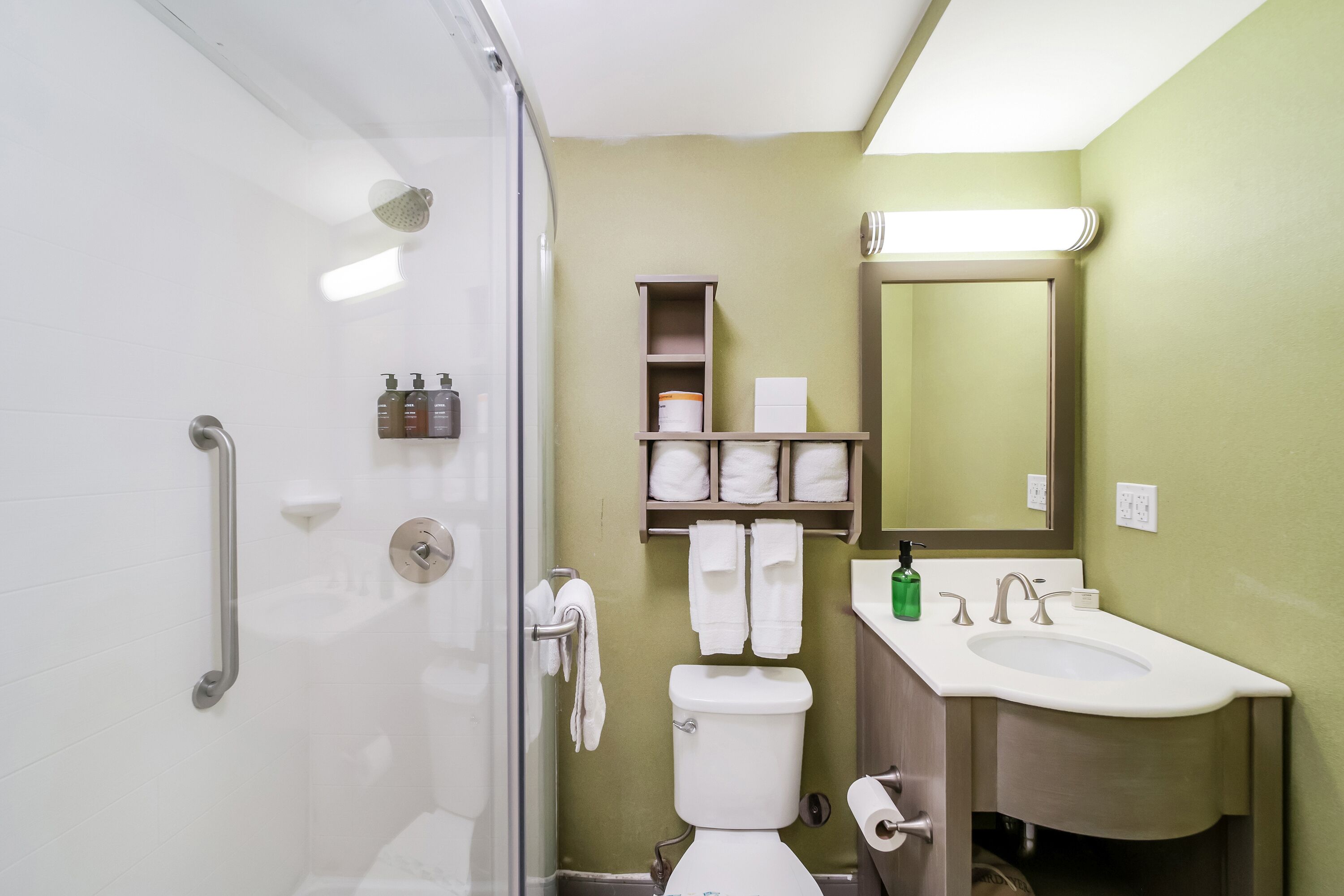 A bathroom with a shower, toilet, sink, and towel storage.