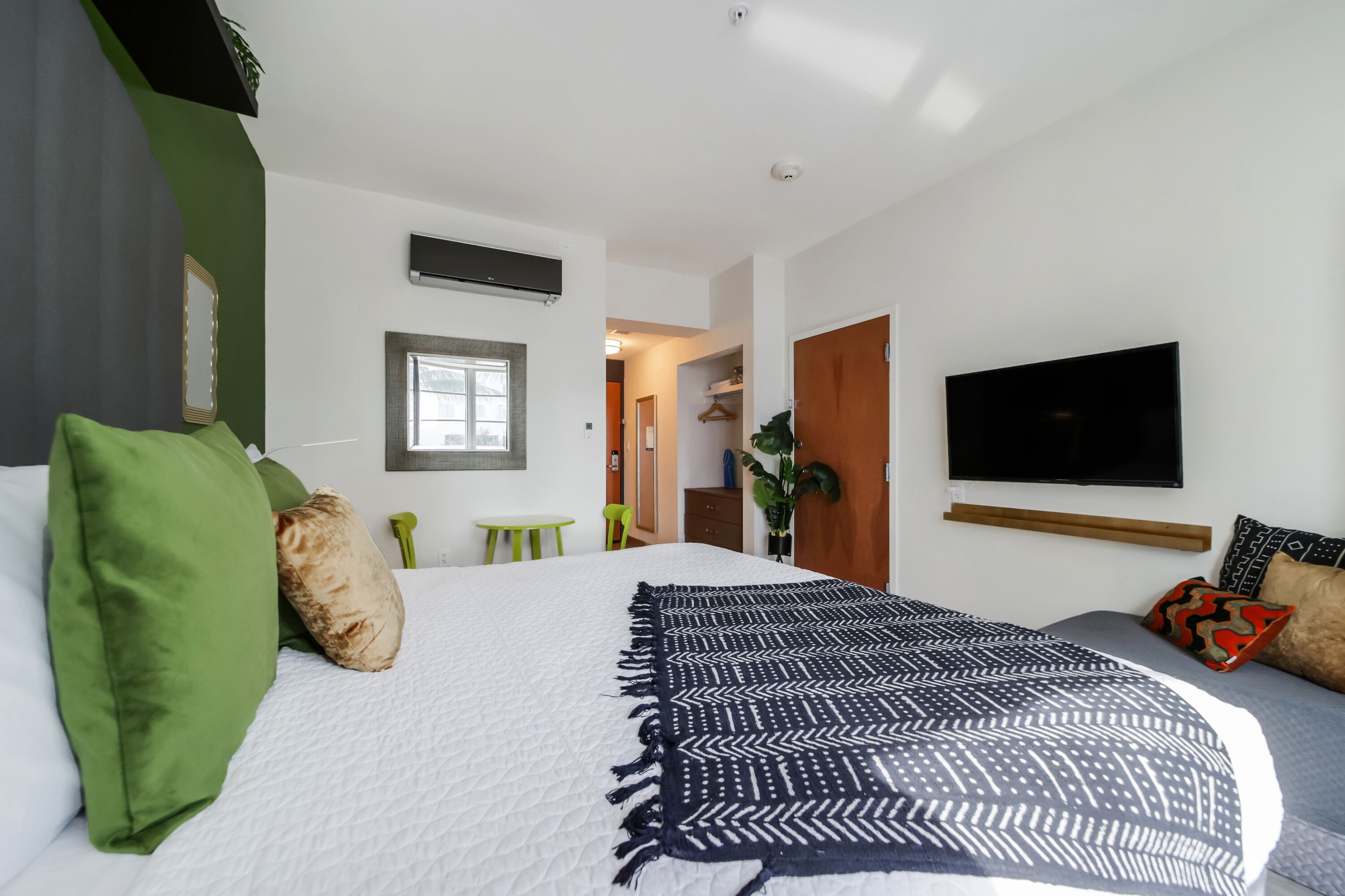 A modern hotel room with a large bed, a flat-screen TV, a small table, and a green chair.