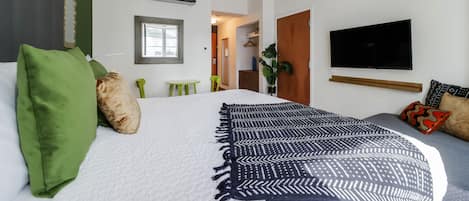 A modern hotel room with a large bed, a flat-screen TV, a small table, and a green chair.