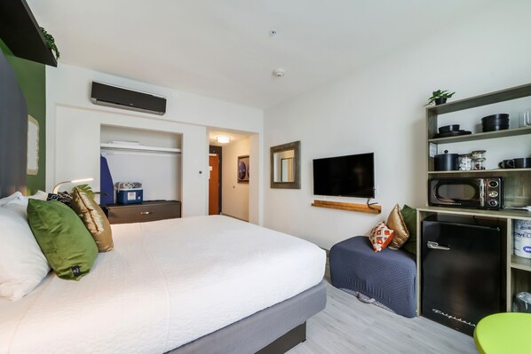Una habitación de hotel con una cama, un escritorio con microondas, televisor y refrigerador.