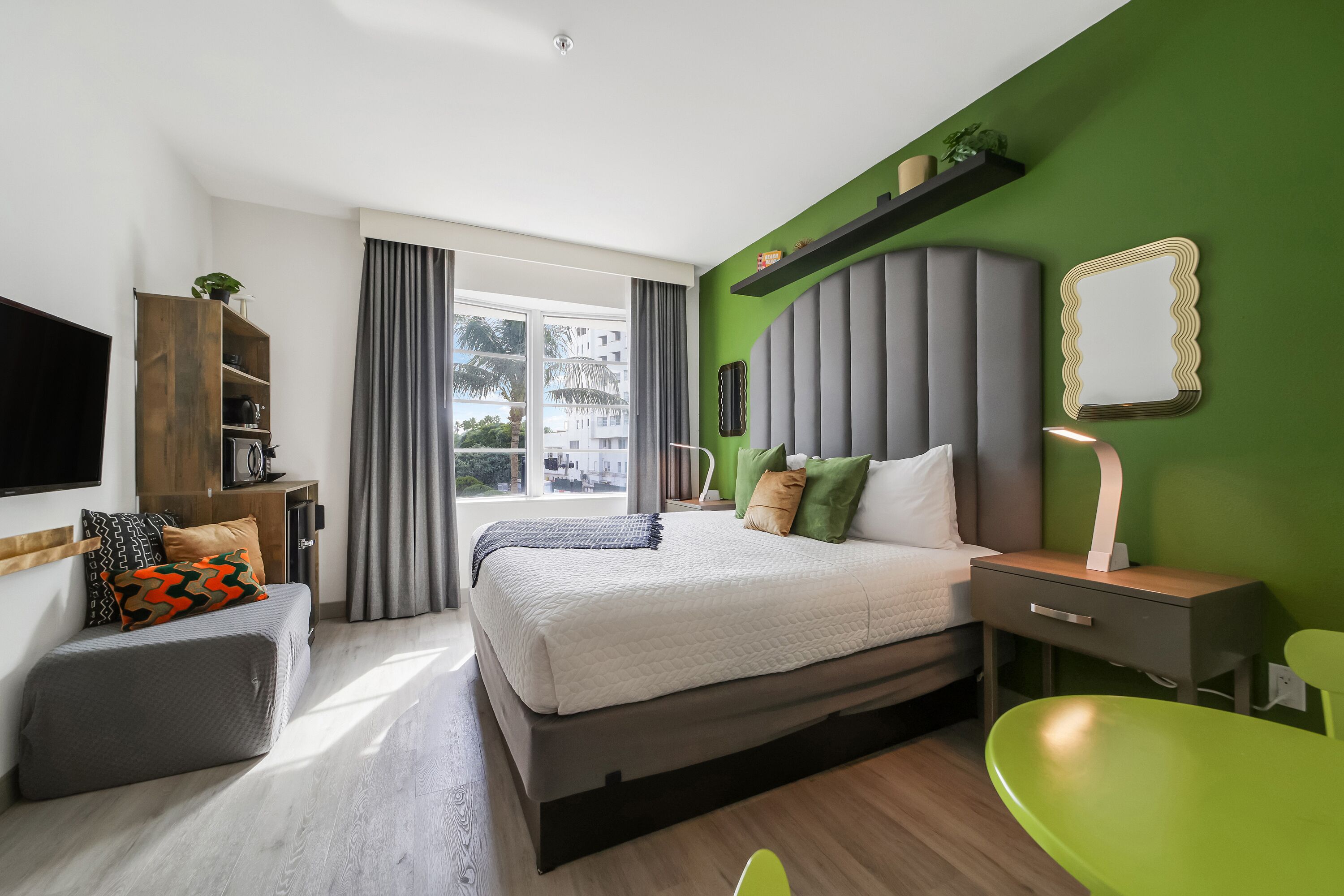 Una moderna camera d'hotel con un grande letto, una scrivania, una poltrona verde e una TV.