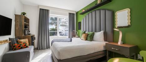 Una moderna camera d'hotel con un grande letto, una scrivania, una poltrona verde e una TV.