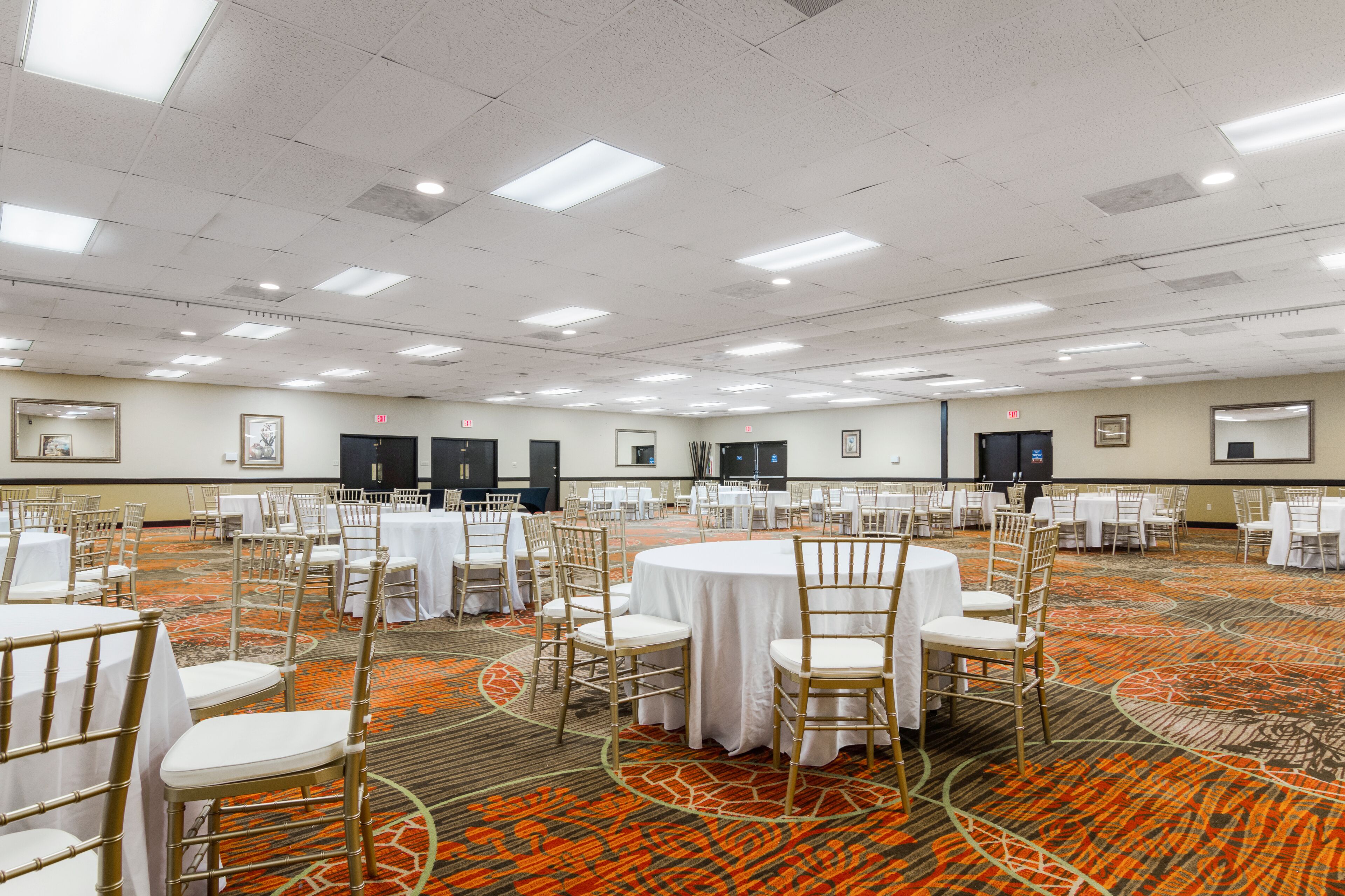 Un'ampia sala conferenze con tavoli e sedie rotonde, pavimento rivestito a moquette e luci a soffitto.