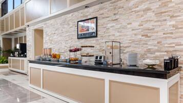 A buffet counter with a stone wall backdrop, a framed menu, and various food and drink dispensers.