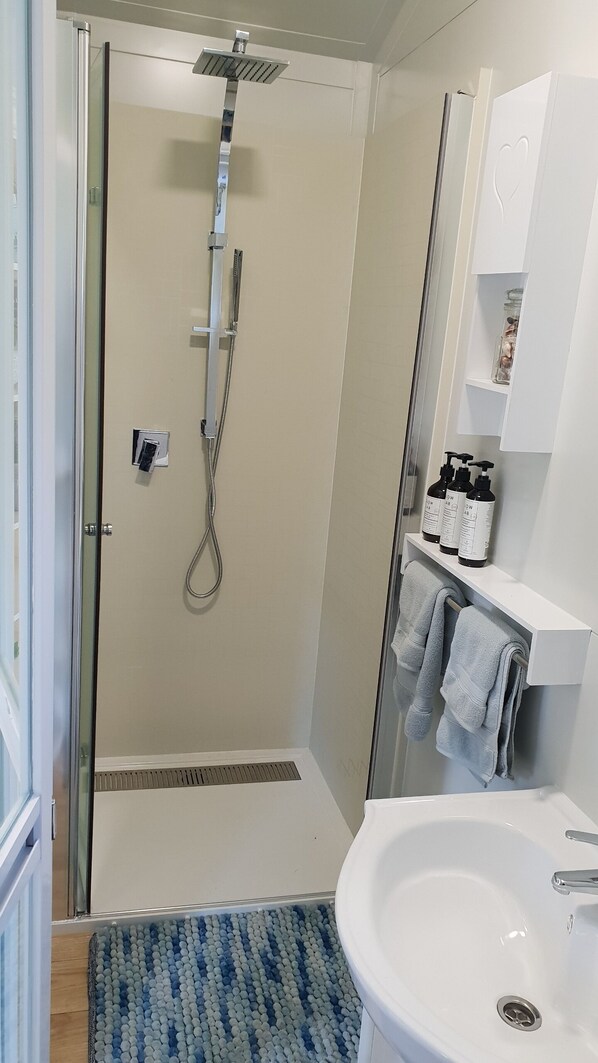 A modern bathroom with a glass-enclosed shower, a white sink, and a towel rack. - Stunning location garden setting, farmstead cottage! (Onamalutu)