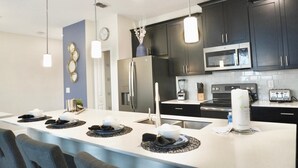 A modern kitchen with dark cabinets, stainless steel appliances, and a central island with seating. - Elegant 4 Bedroom Getaway w/Private Pool 114 (ChampionsGate)