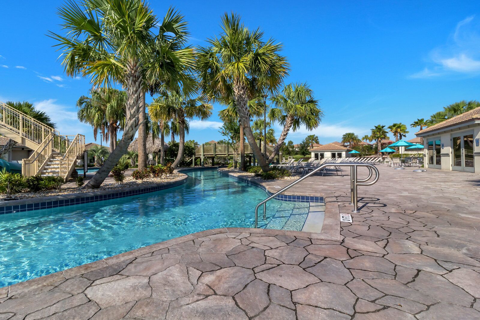 Una piscina con baldosas de piedra, palmeras y sillones de descanso.