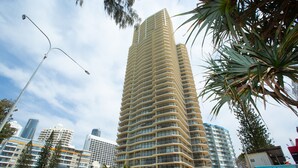 A tall, modern high-rise building with a curved facade, surrounded by other high-rise buildings and palm trees.